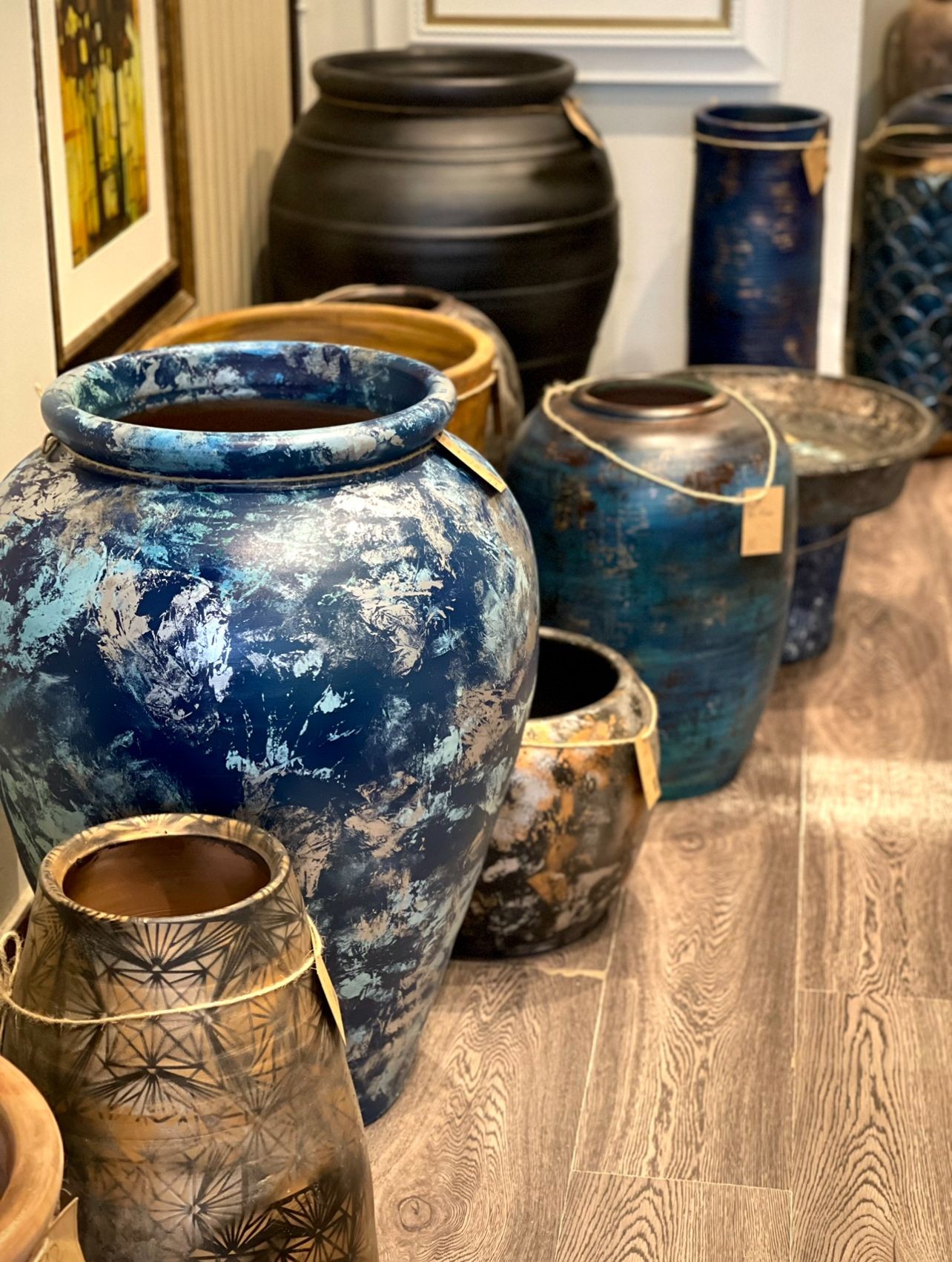 Collection of large decorative vases and pottery in various colors and designs displayed on a wooden floor.