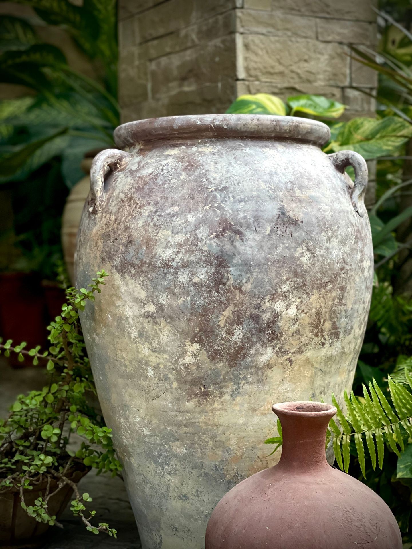 Two large weathered clay pots placed outside in a garden setting with green plants in the background.