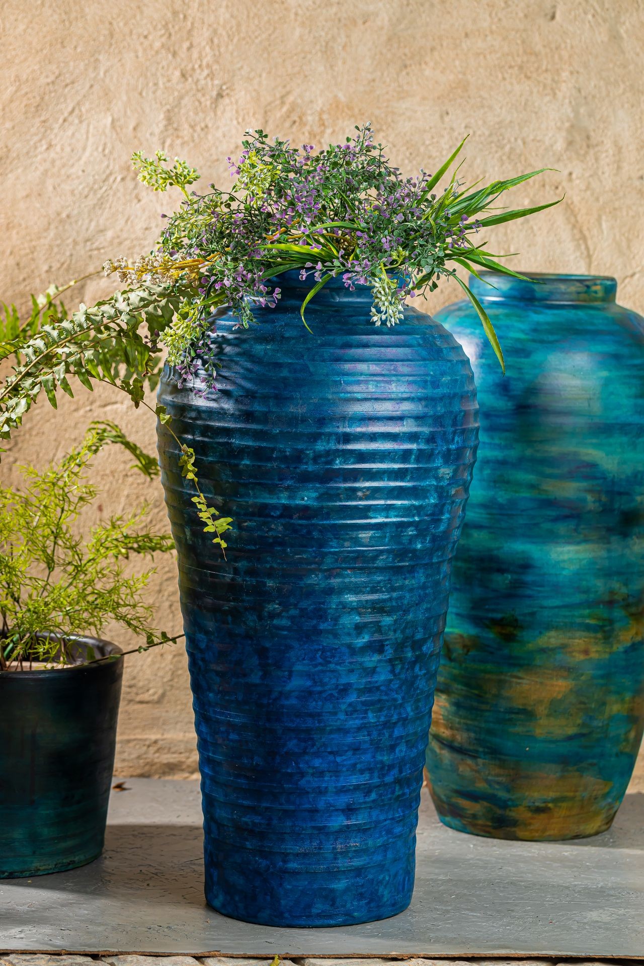 Blue ceramic vase with decorative foliage and flowers, set against a beige textured wall.