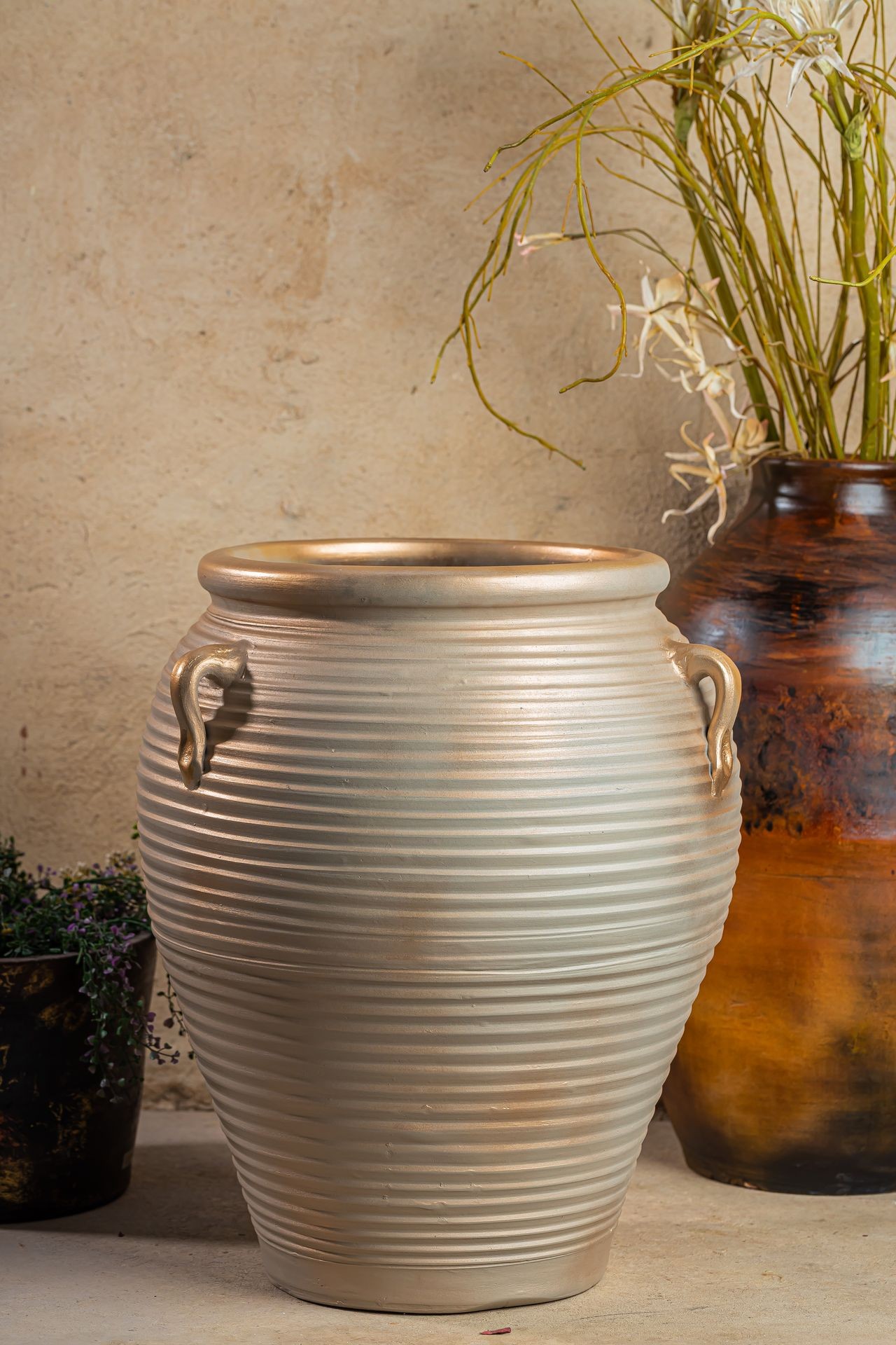 Large textured ceramic vase with handles, placed near another ceramic pot filled with dry branches and flowers.