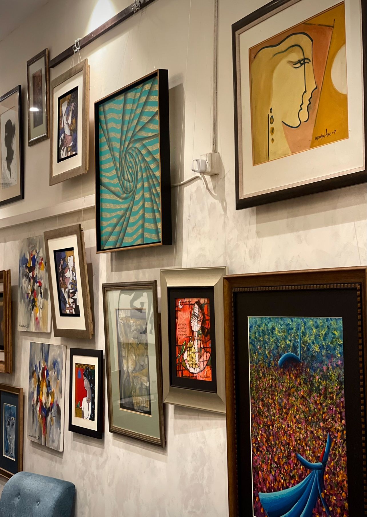 Gallery wall displaying various framed artworks including abstract paintings, portraits, and colorful designs.